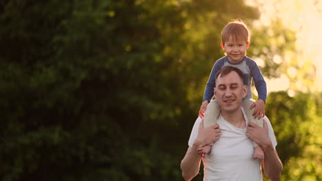 Loving-father-smiles-walking-with-the-child-sitting-on-the-neck-at-sunset-on-a-meadow-in-summer-in-slow-motion.